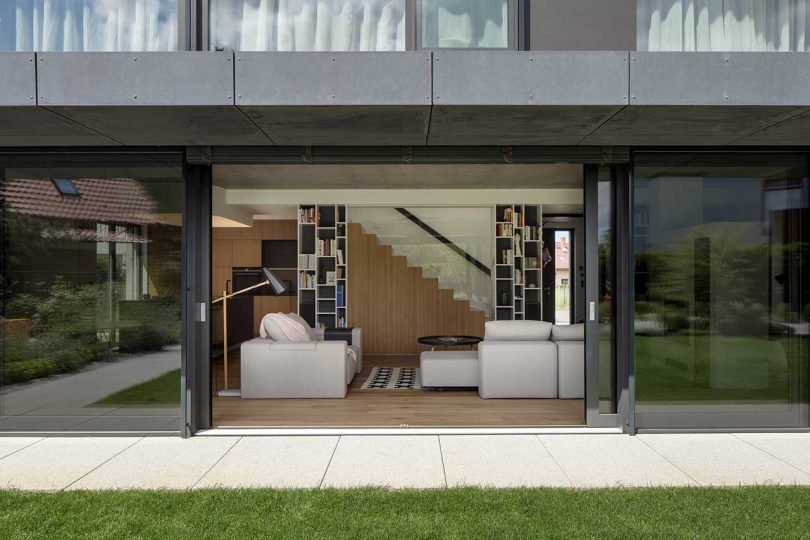 looking from outside in to modern living room in concrete, wood, and white surfaces