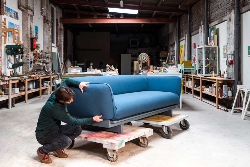 Man squatting next to blue sofa on cart