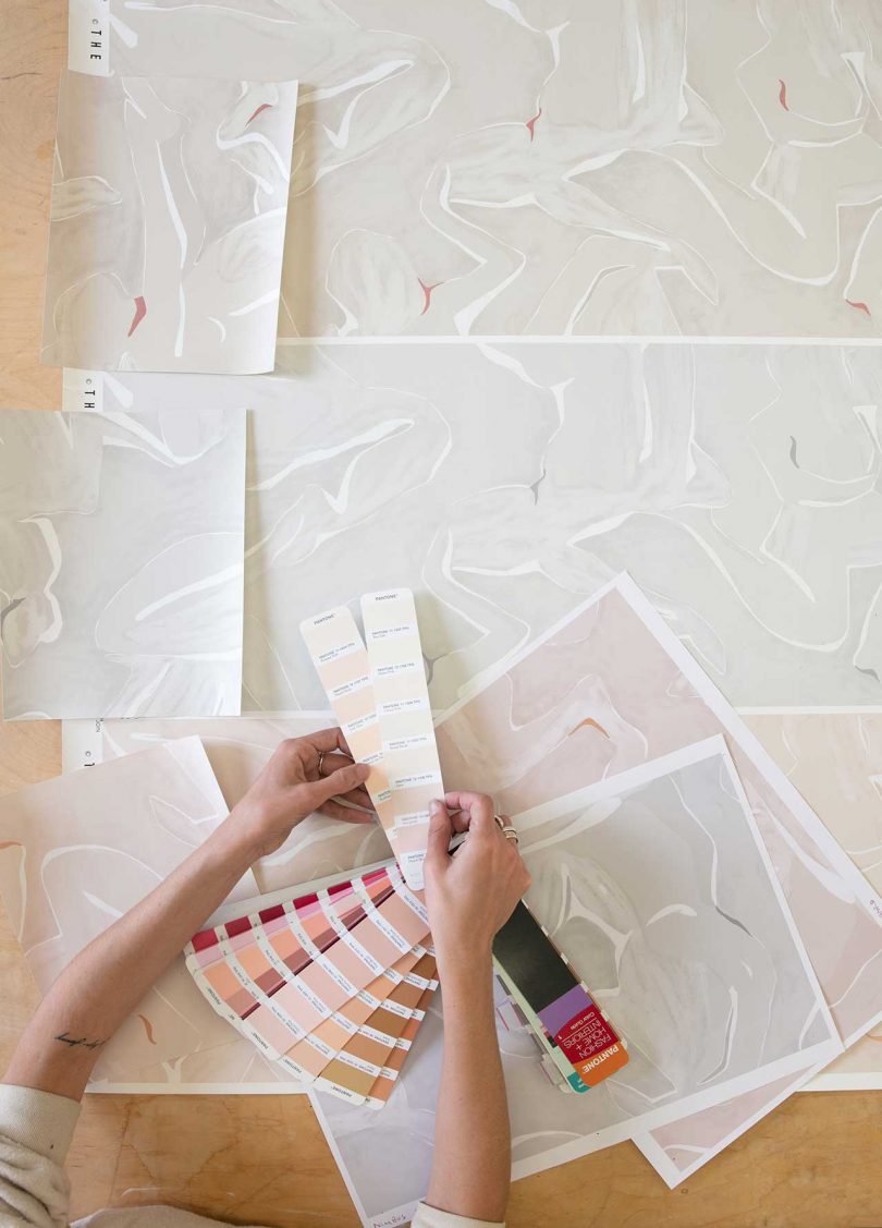 artist's hands holding paint chips over abstract drawings