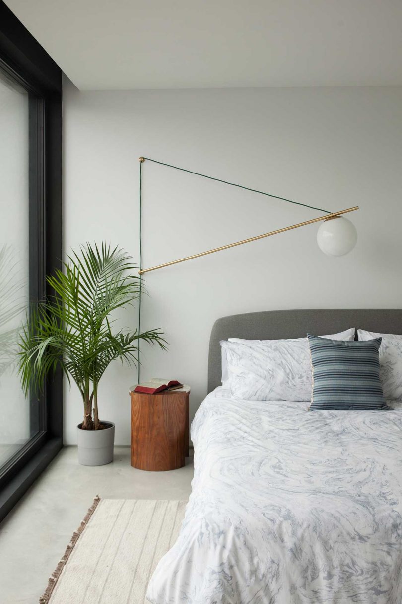 view of half of a bed with light bedding and geometric lamp