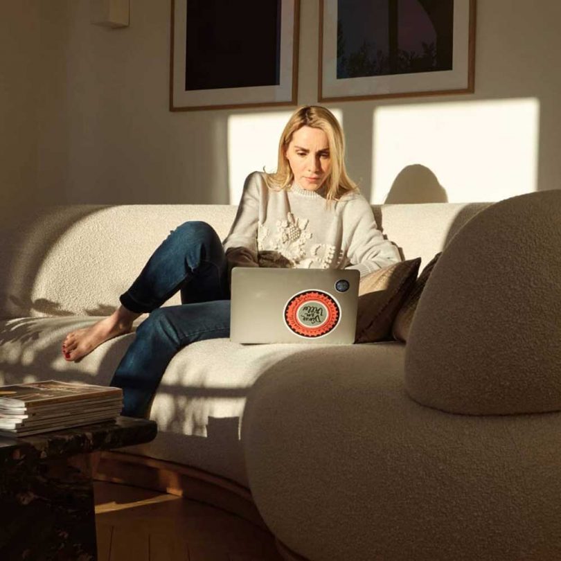 woman working on laptop on cream sofa with sunlight coming through windows