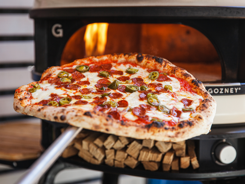 cooked pizza being removed from pizza oven