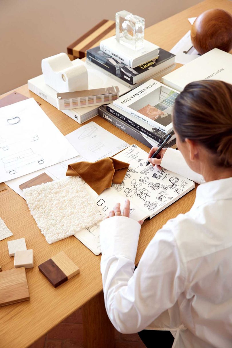 angled view of designer at desk sketching in notebook with textile sample around