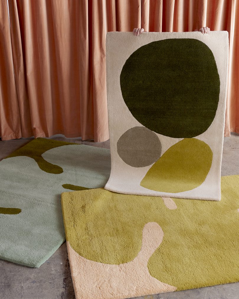 three colorful abstract floor rugs in front of hanging pink curtain