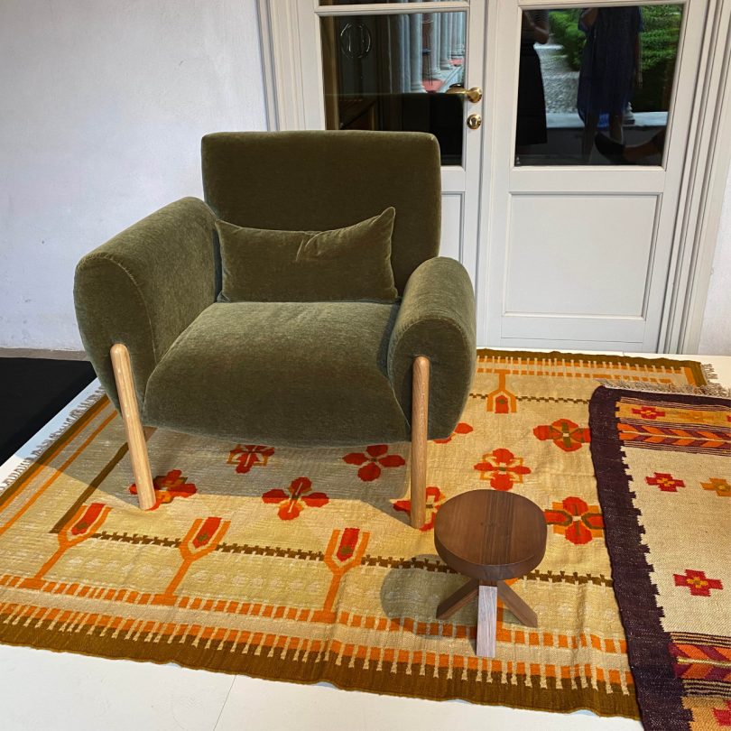 upholstered modern lounge chair in dark green velvet with armrests at two heights over a patterned rug