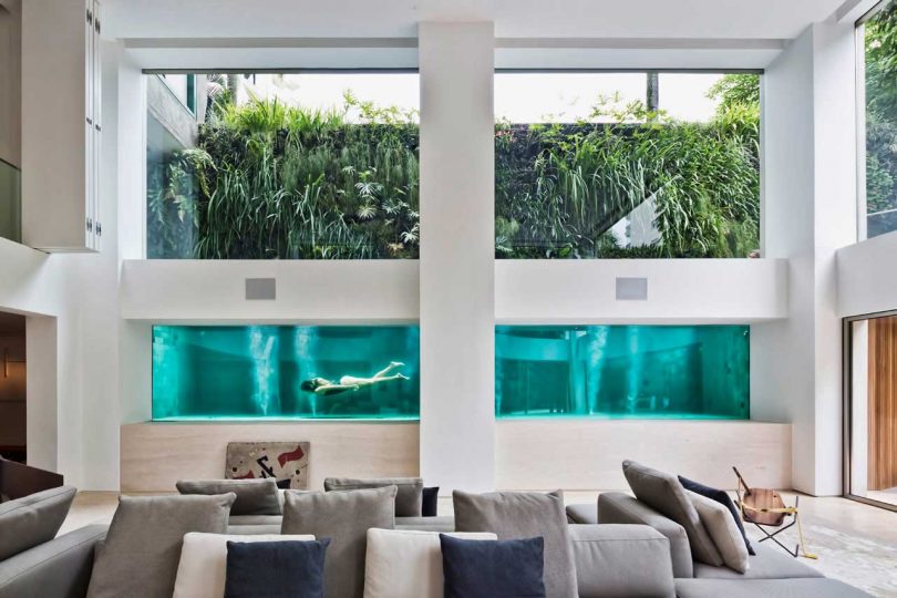 interior view from modern living room looking through windows into a swimming pool where people are swimming