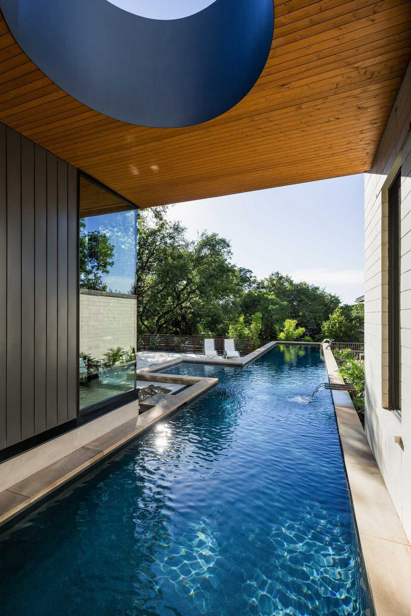 outside view of modern home with elongated pool that extends out from a covered patio