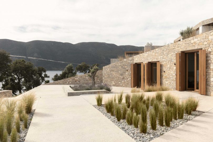 exterior side view of stone clad house surrounded by pathways and native landscaping