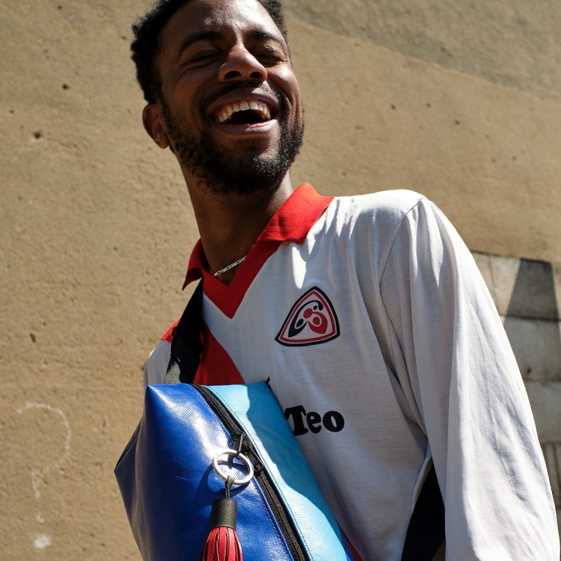 man from waist up laughing with crossbody blue and turquoise bag