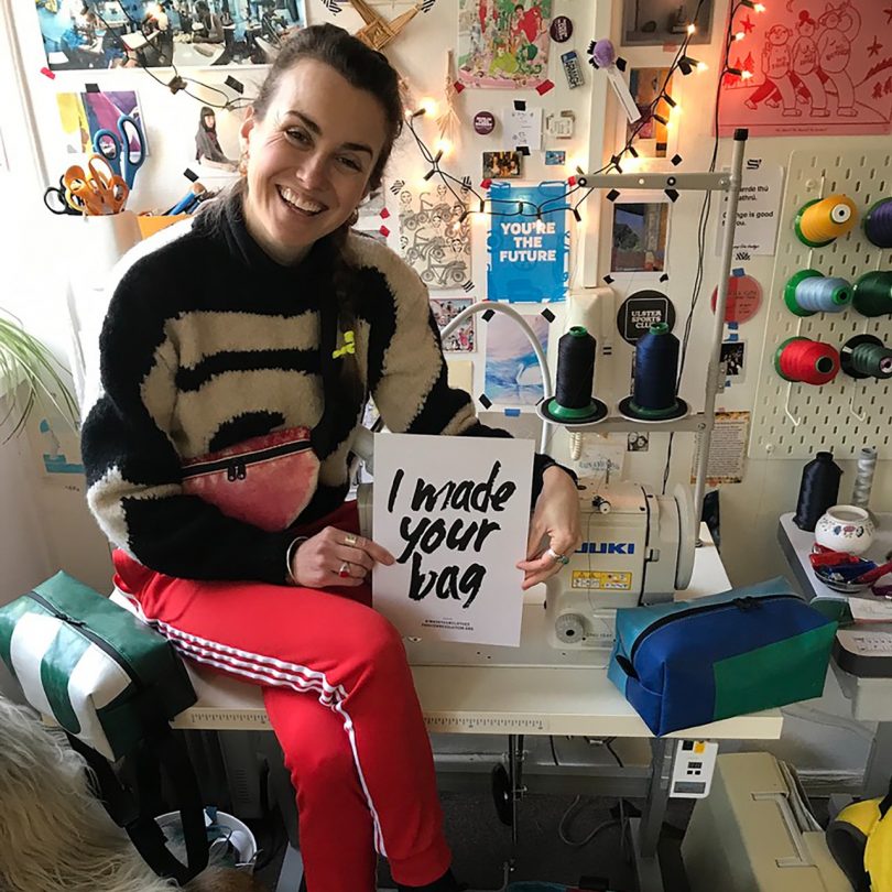 woman sitting with smile on face holding a sign saying "i made your bag"