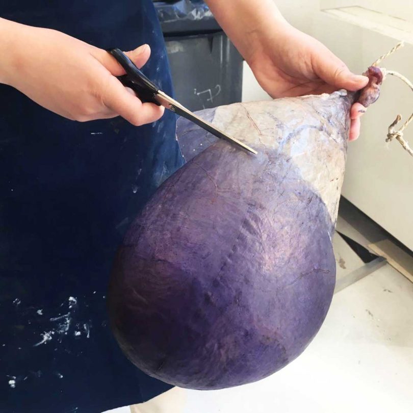 two hands holding and cutting purple balloon-like material