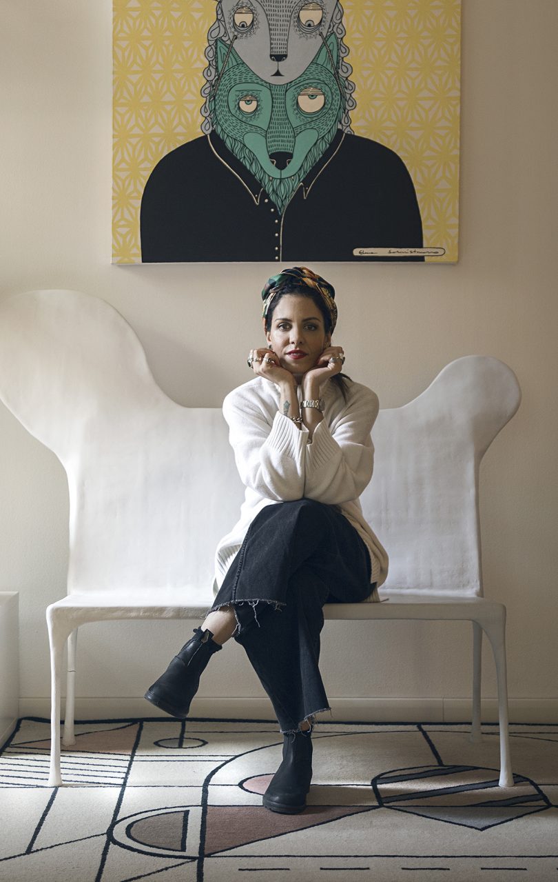 brown-skinned woman sitting on a modern chair with her legs crossed and her face resting on her hands