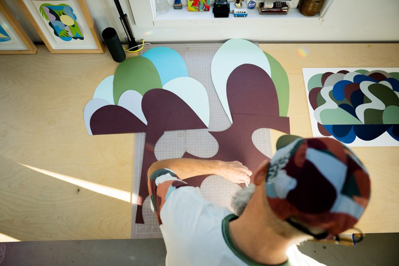 Artist Travis Weller from overhead shown cutting pieces of colored paper for composition..