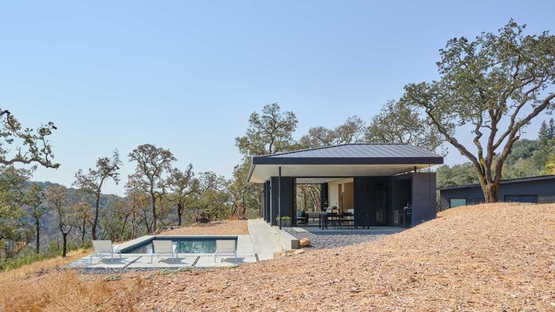 side view of small modern black house open to outdoors on sloped land