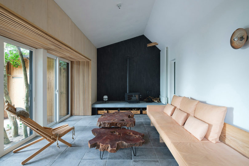 Interior cabin living space within the Sumu Yakushima is a co-operative housing project, with sofa and chairs near fireplace in background.