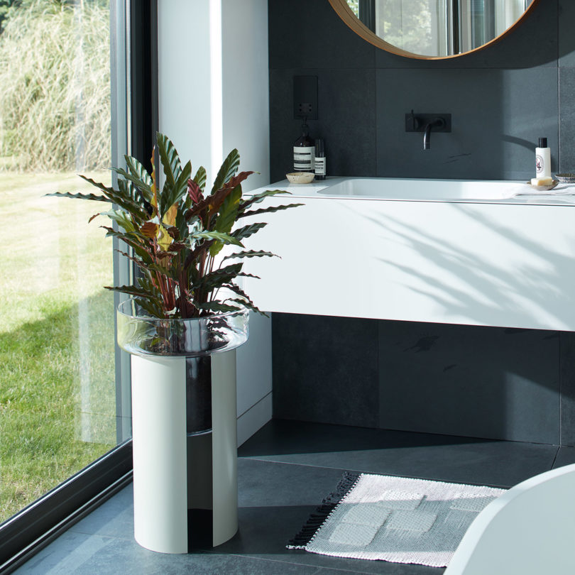 self-watering glass planter on the floor in a bathroom