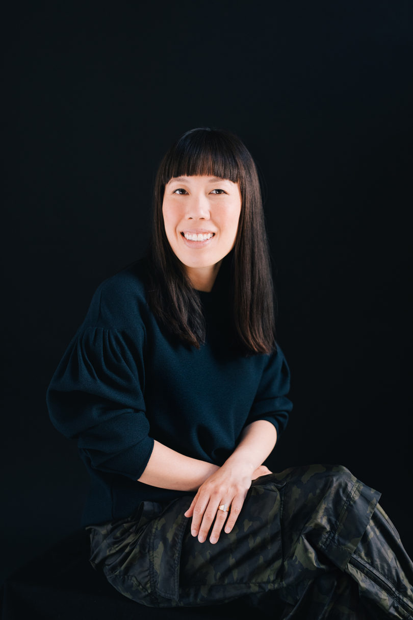 light-skinned woman with long dark hair wearing a black shirt against a black background