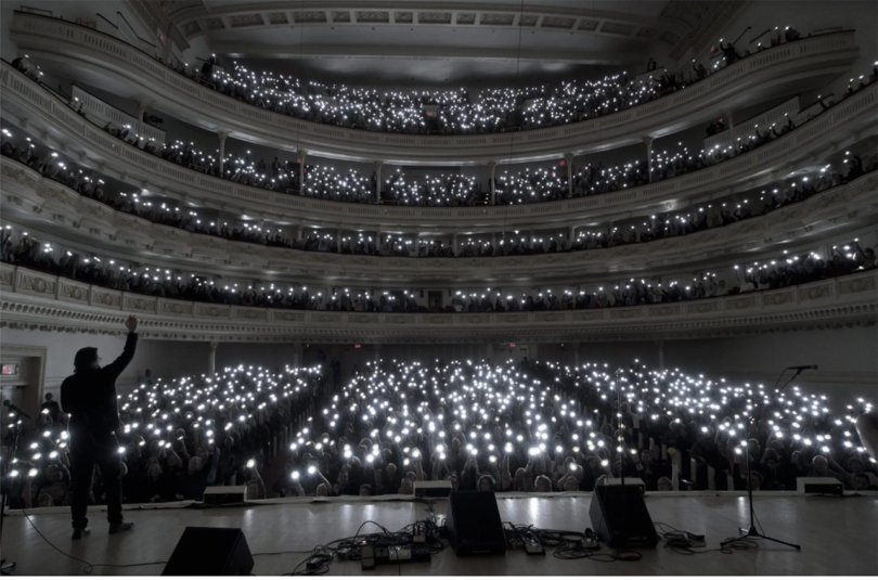 black and white photo looking out onto an audience of white lights