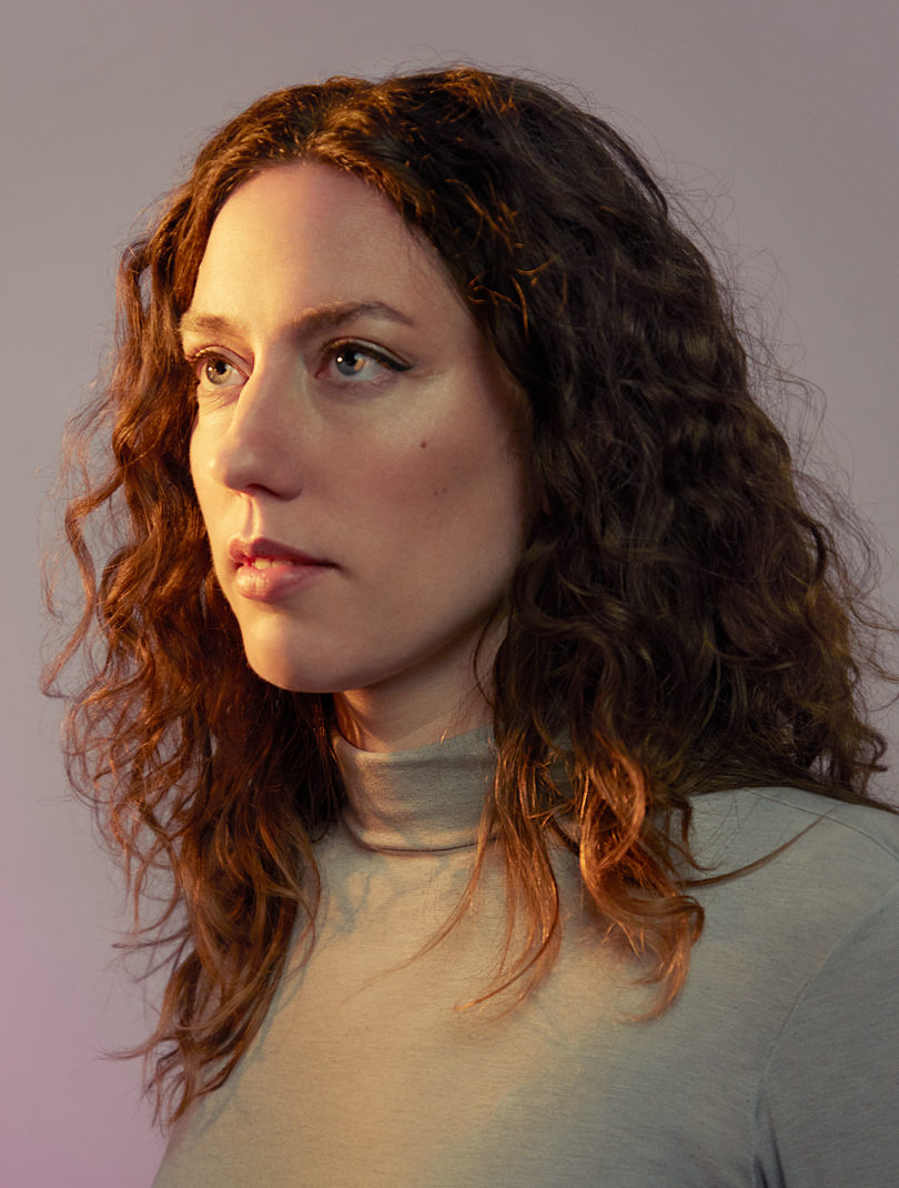 light-skinned woman with long, curl auburn hair posting for a portrait