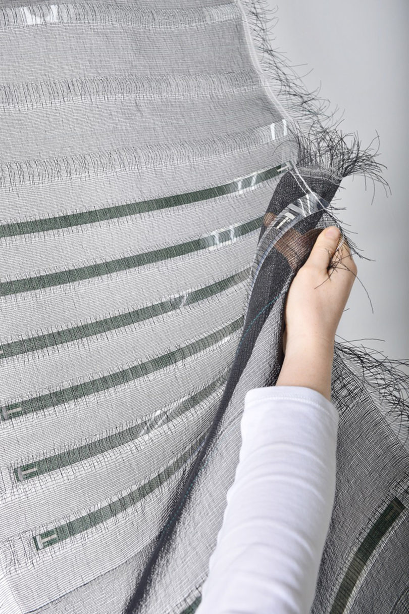 light-skinned hand examines a piece of light grey textile