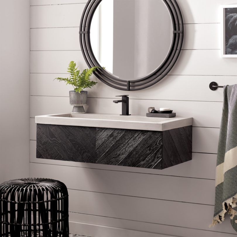 A circular mirror with a black frame sits above a suspended white sink on a black frame.