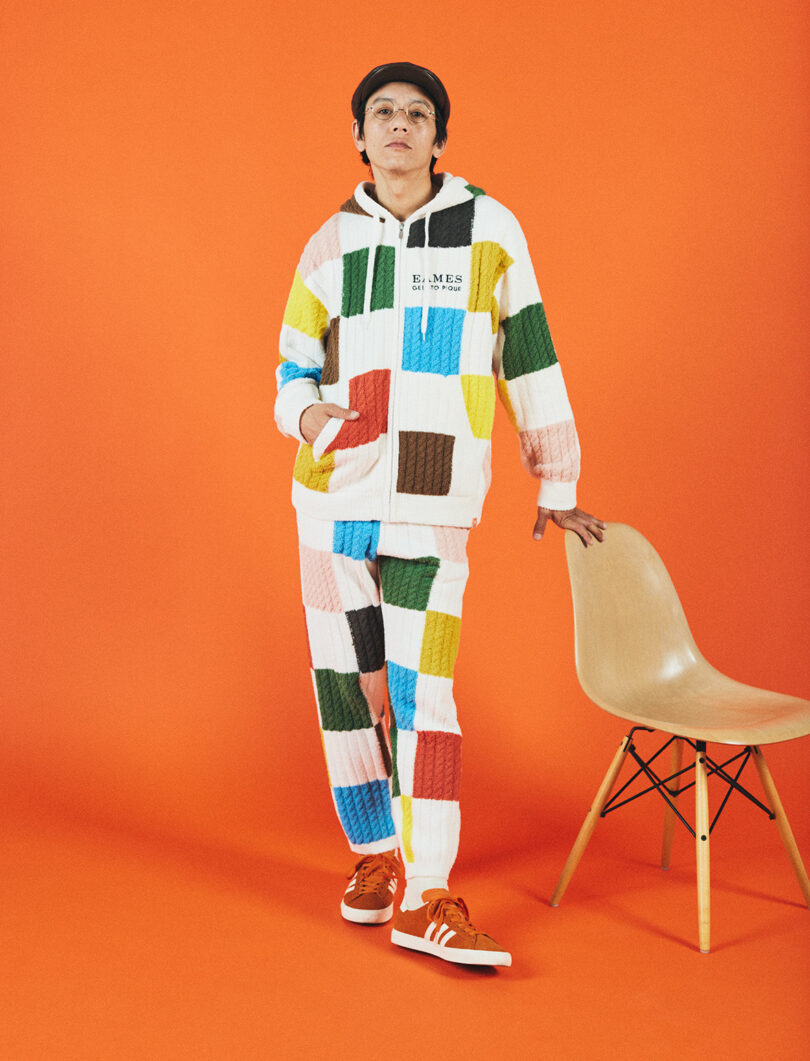 man standing with hand on chair in a checkered lounge suit on orange background