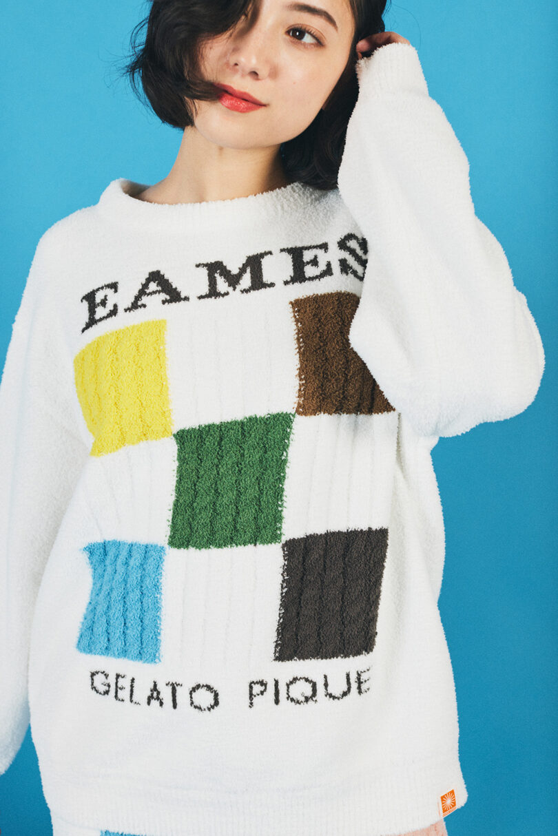 woman standing with hand in hair wearing white sweater with eames and checkers