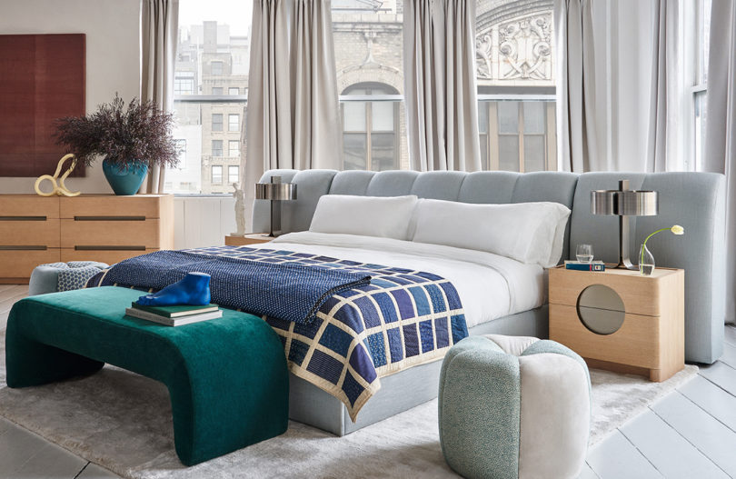 styled interior space with upholstered bed, bench, ottoman, dresser, and bedside tables