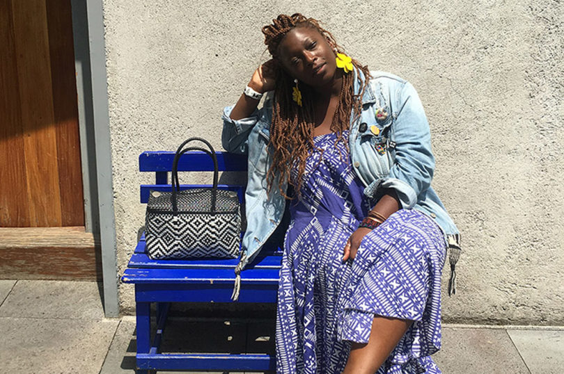 brown-skinned woman with long hair wearing bright, patterned clothing while sitting on a blue bench