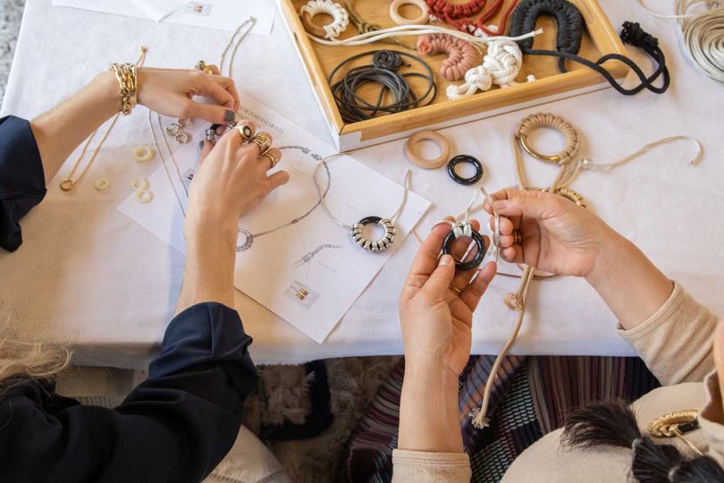 view down onto a work table with two sets of hands making jewelry