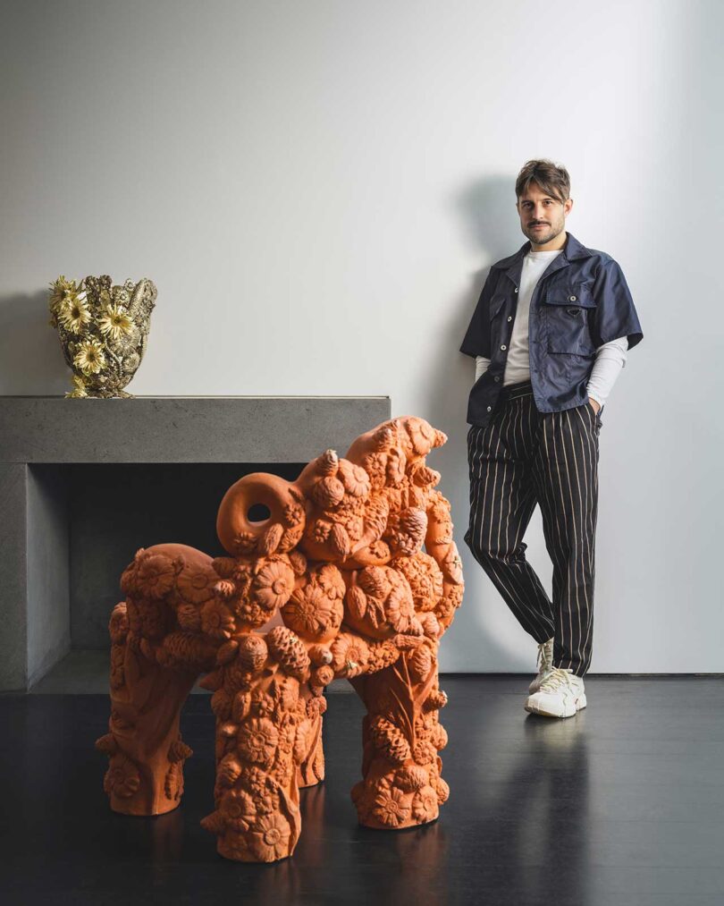 man standing against a back wall with large terracotta sculpture in front