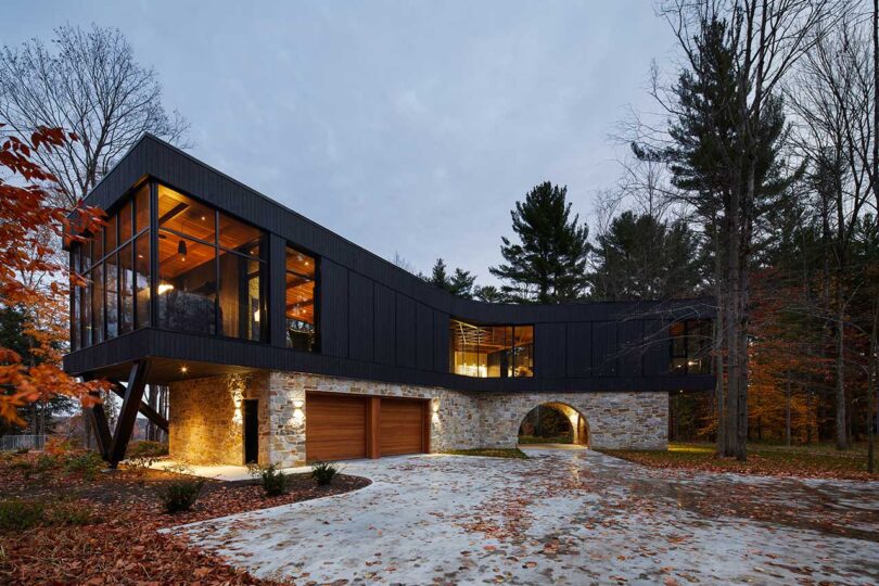 elongated exterior view at twilight of modern house with stone ground level and wood and glass upper level