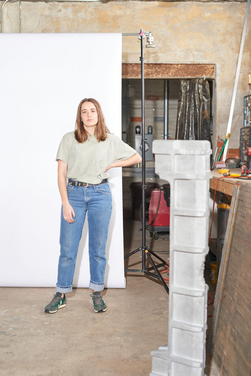 light-skinned woman wearing jeans and a t-shirt stands with her hand on her hip in the middle of her studio