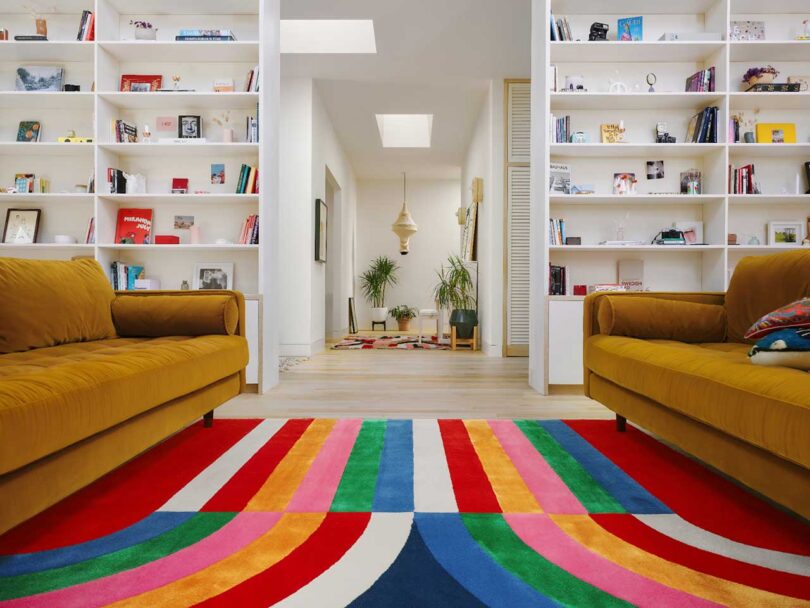 middle view of modern living room with two gold sofas facing each other and colorful striped rug in center