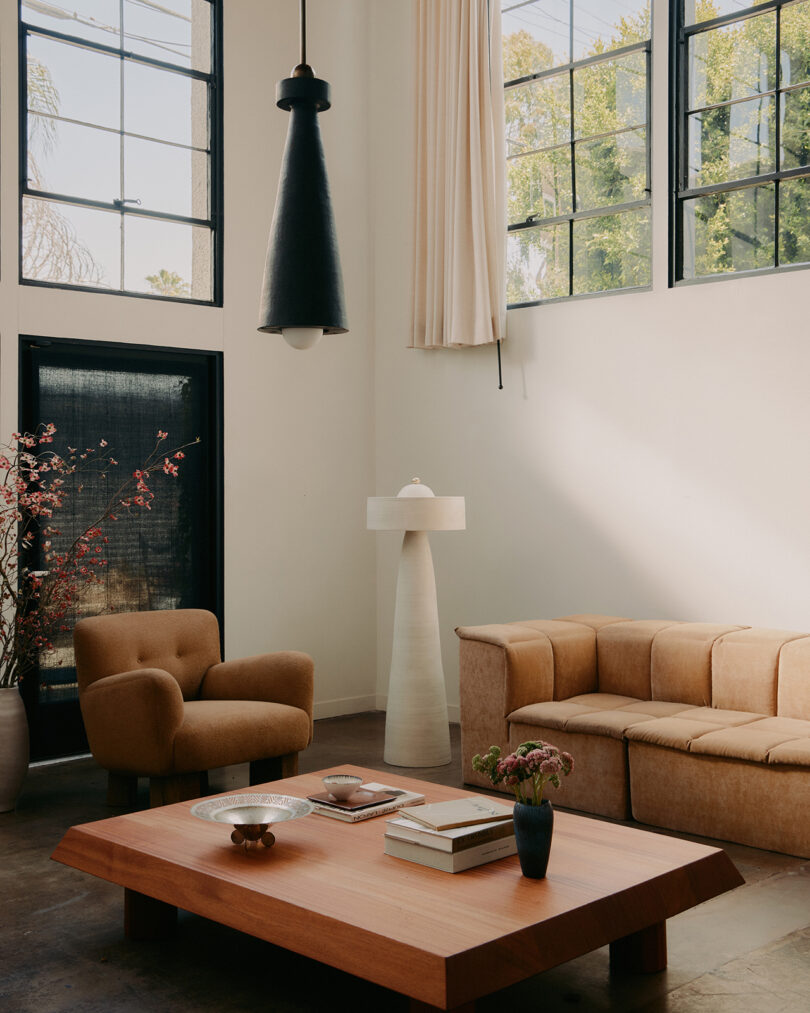 styled interior space with sofa, coffee table, white floor lamp, black pendant lamp, and windows