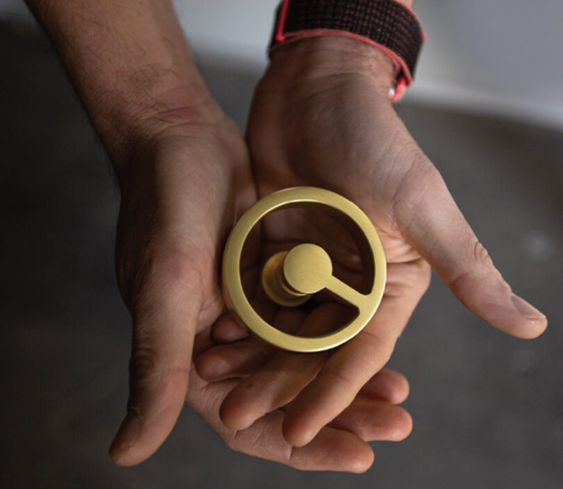 two hands holding a spoke-shaped bronze door pull