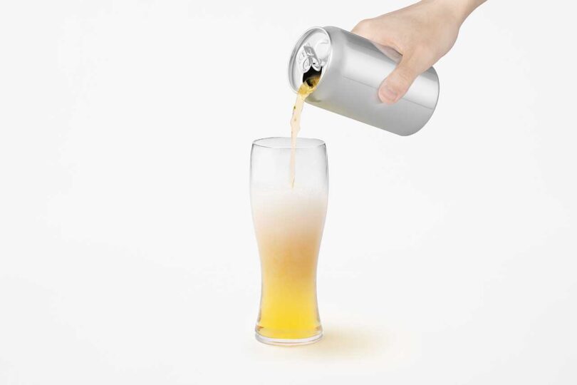 chrome beer can held in hand pouring beer into glass