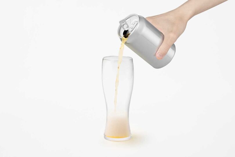 chrome beer can held in hand pouring beer into glass