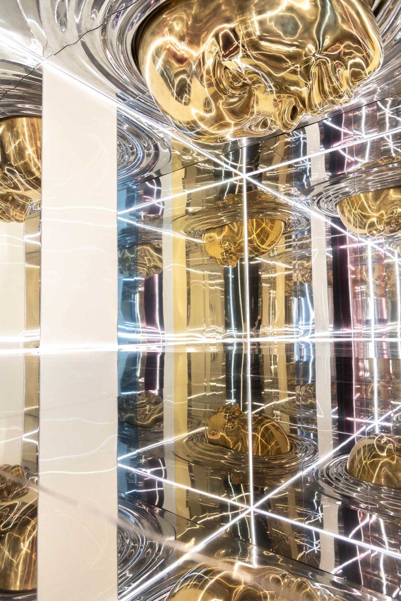 angled view of mirrored installation with gold faces and linear lights in white