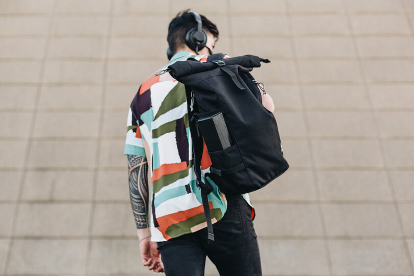 light-skinned person wearing a bold geometric short-sleeved shirt and carrying a black backpack