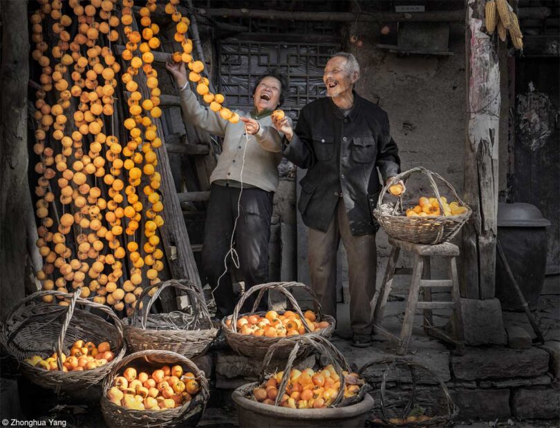 man and woman surrounded by baskets of orange persimmons while hanging some