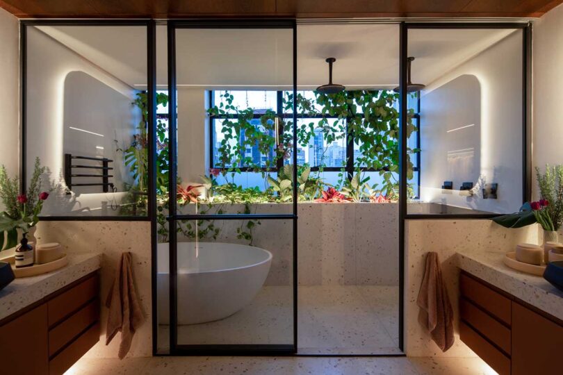 view of modern bathroom with vanities on either side and shower and tub behind sliding glass doors in front of window