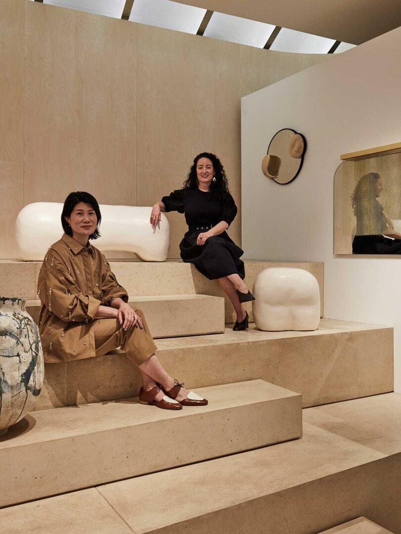 Two women sitting on stadium platform amongst artwork on display