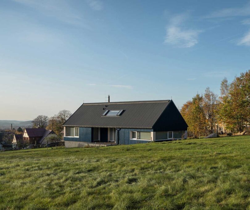 exterior angled view of blue modern cabin in green field