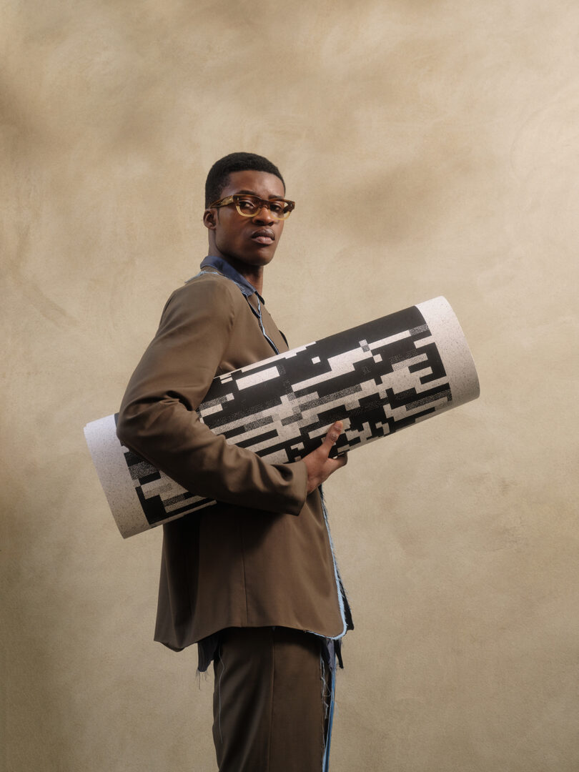 brown-skinned man with glasses holds a rolled up black and white screen print