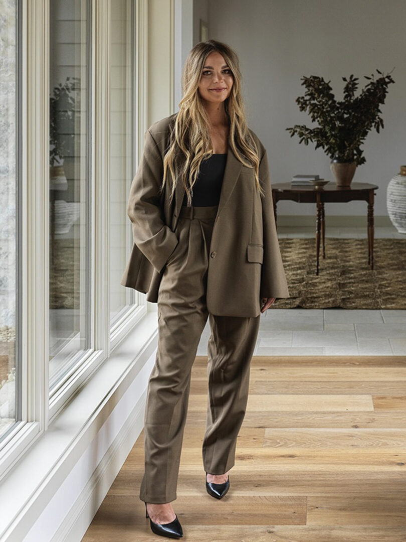 light-skinned woman with long blonde hair wearing dark olive green suiting and standing with her hand in her pocket