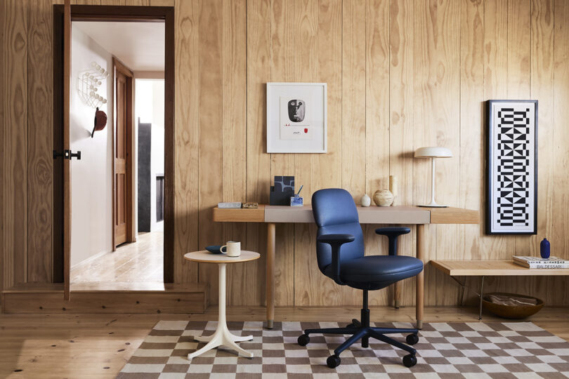 Asari task chair in black in a living room home office setting with wood panel walls and checkered rug with doorway door open to the left.