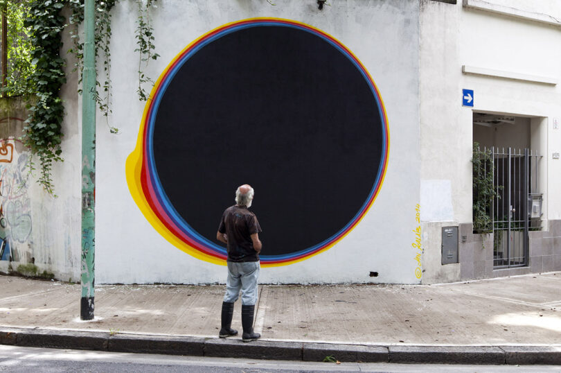 large black graffiti circle with rings of primary colors around it as an observer stands by