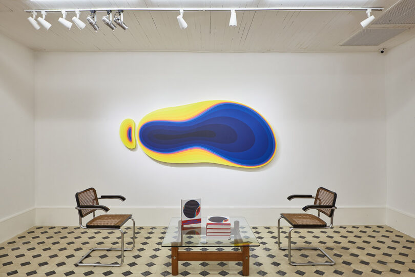 amorphous yellow and blue shape hangs on a wall surrounded by seating and a coffee table