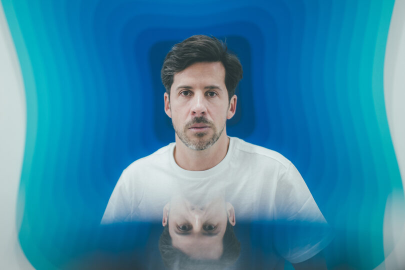 light-skinned man with dark hair wearing a white t-shirt surrounded by a haze of blue